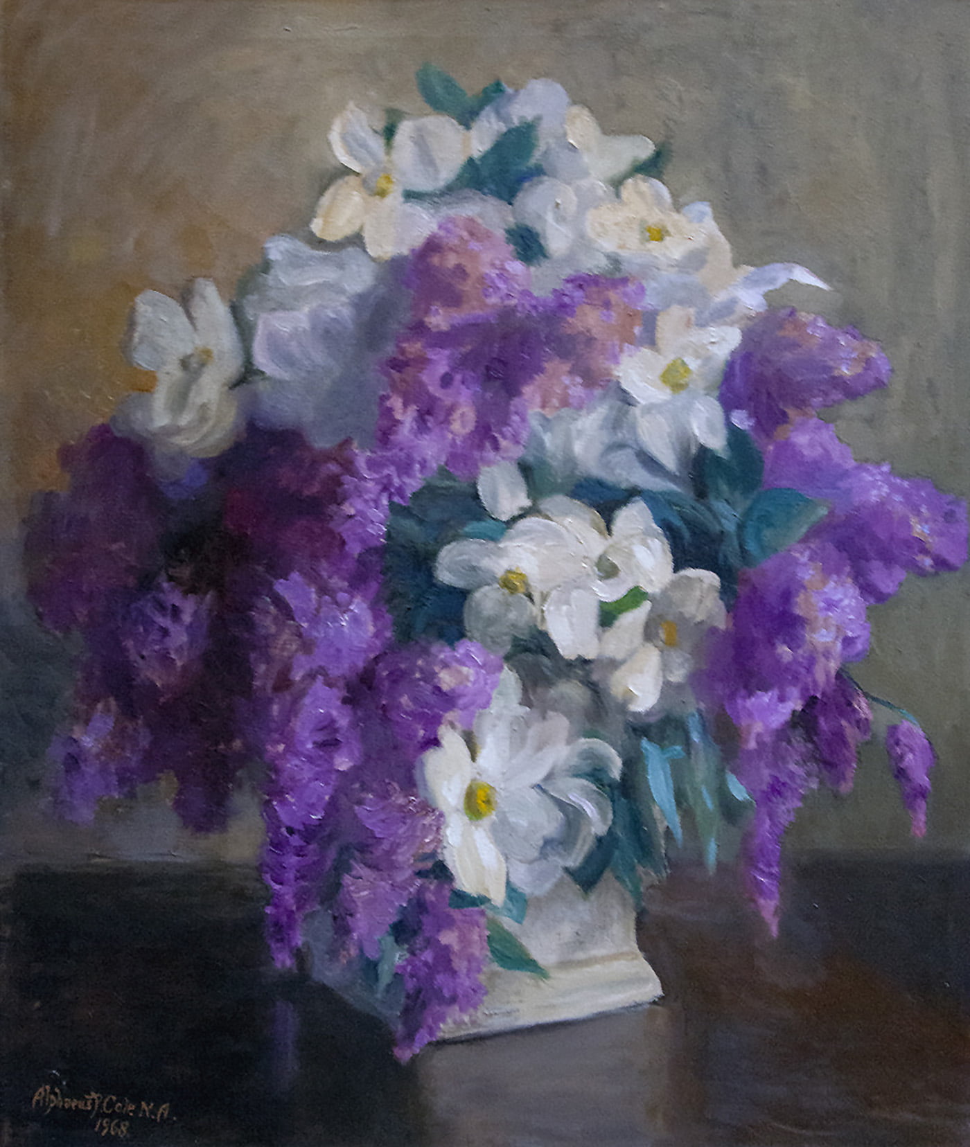 White daisy-like flowers and droopy light purple blossoms nearly cover up the white vase they are in.