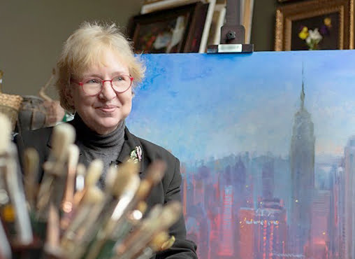 a woman sitting in front of a painting of a city.