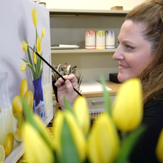 a woman is painting a picture with yellow tulips.