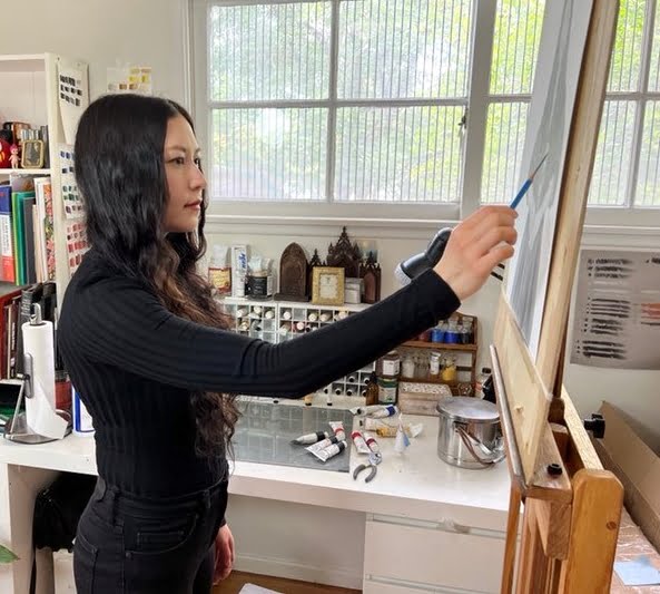 a woman standing in front of a easel holding a paintbrush.
