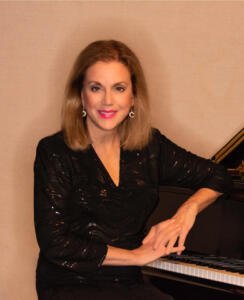Nancy Winston sitting at a piano with a smile.