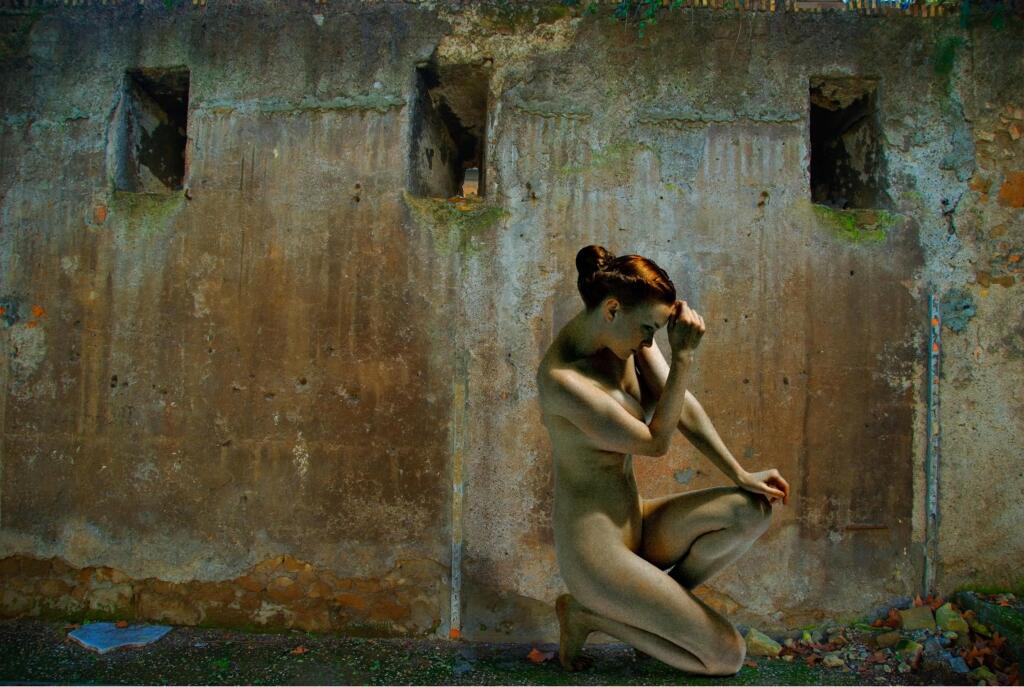 A digitally manipulated photographic piece; a nude woman kneels down on one leg against a crumbling wall.