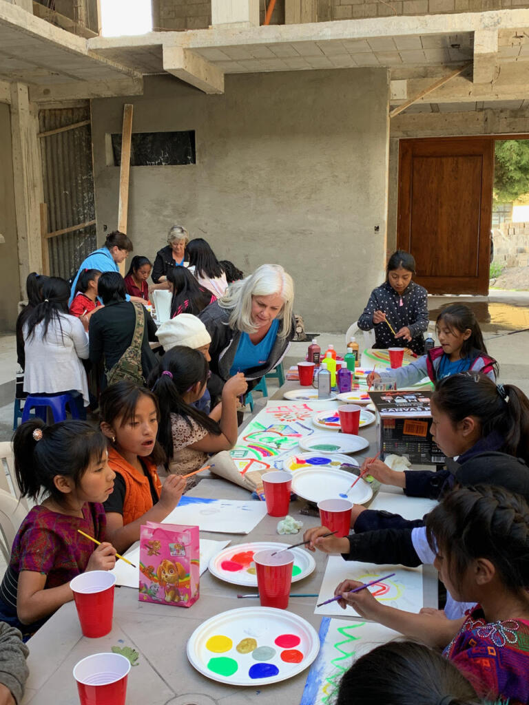 An art class is held amongst Eastern children. There are plates serving as palettes of acrylic paints and red cups of water.