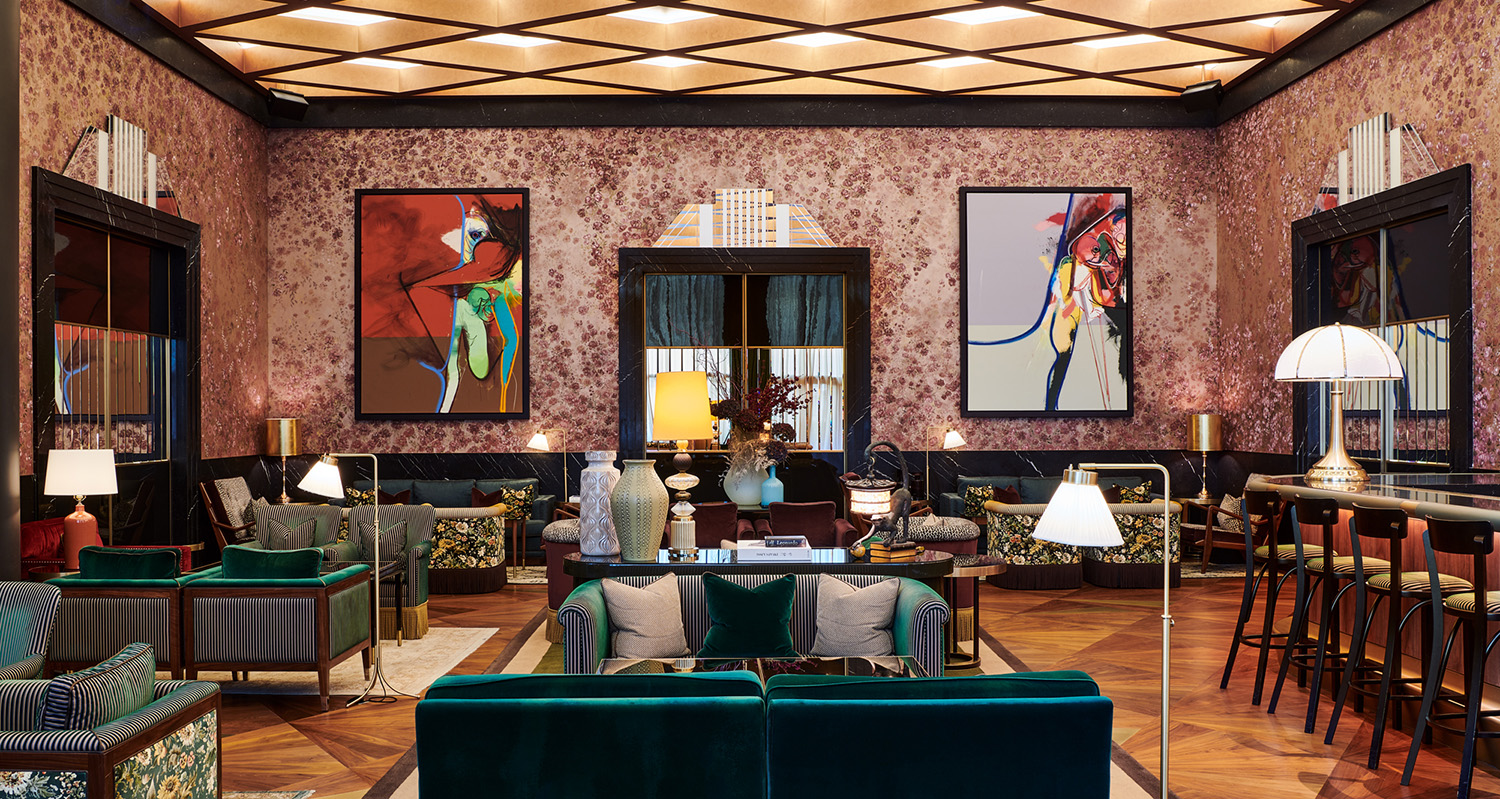 There is a variety of textures and patterns in the interior of The Arts Club in Dubai. A pair of colorful abstract paintings hang on rose-tinted walls, with chairs of florals and emerald.