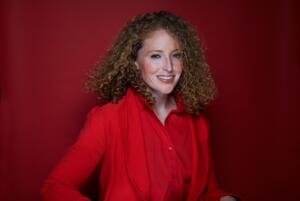 Marissa Mulder is a woman with curly hair wearing a red blouse.