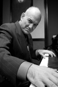 Black and white: Bill Zeffiro is a bald man in a suit playing a piano.