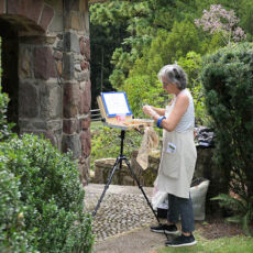 a woman is painting in a garden setting.