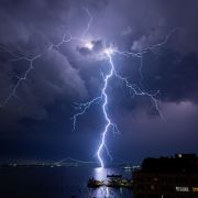 A lightning bolt hitting the water near a city at night.