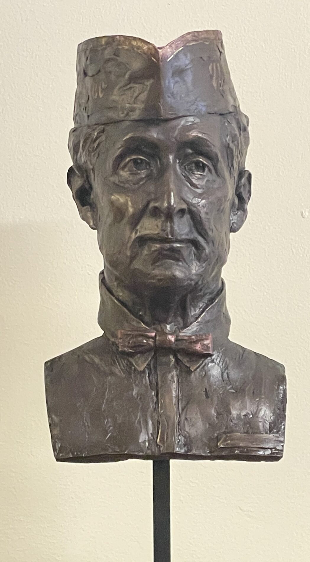 Dark bust of a slim middle-aged man wearing a sailor's hat and thin bow tie.
