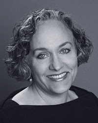 In black and white: Claudia G. Jaffe is a middle-aged woman with chin-length curly hair, wearing a high-cut, wide square neckline.