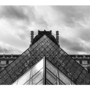 Black and white: looking up at the pyramidal structure at the front of the Louvre on a cloudy day.