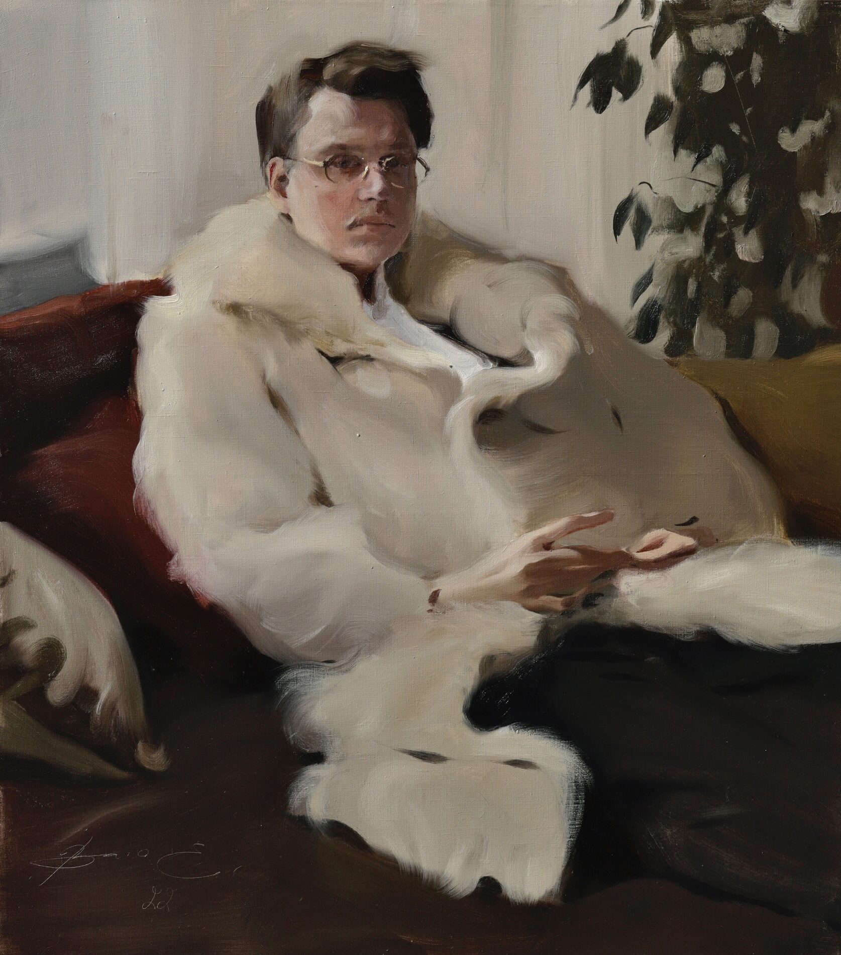 A man in a white fur coat and glasses sits on a couch.