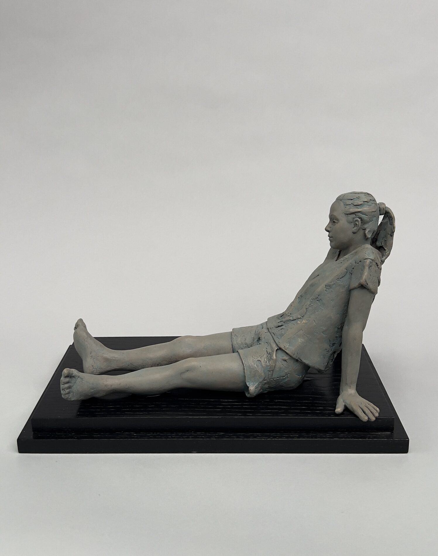 A gray sculpture of a girl sitting with her legs out in front of her.