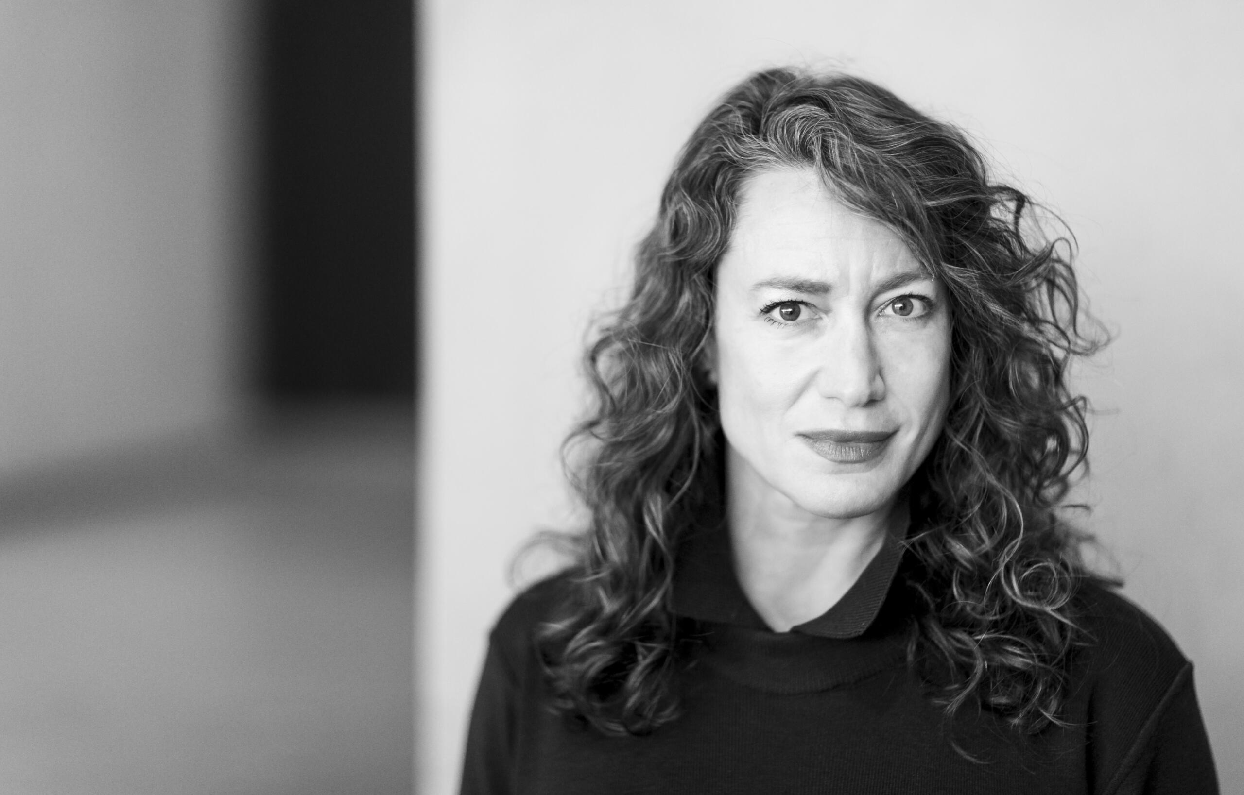 Lauren Sandler, from the shoulders up, in black and white, in a curly-haired, slim woman.