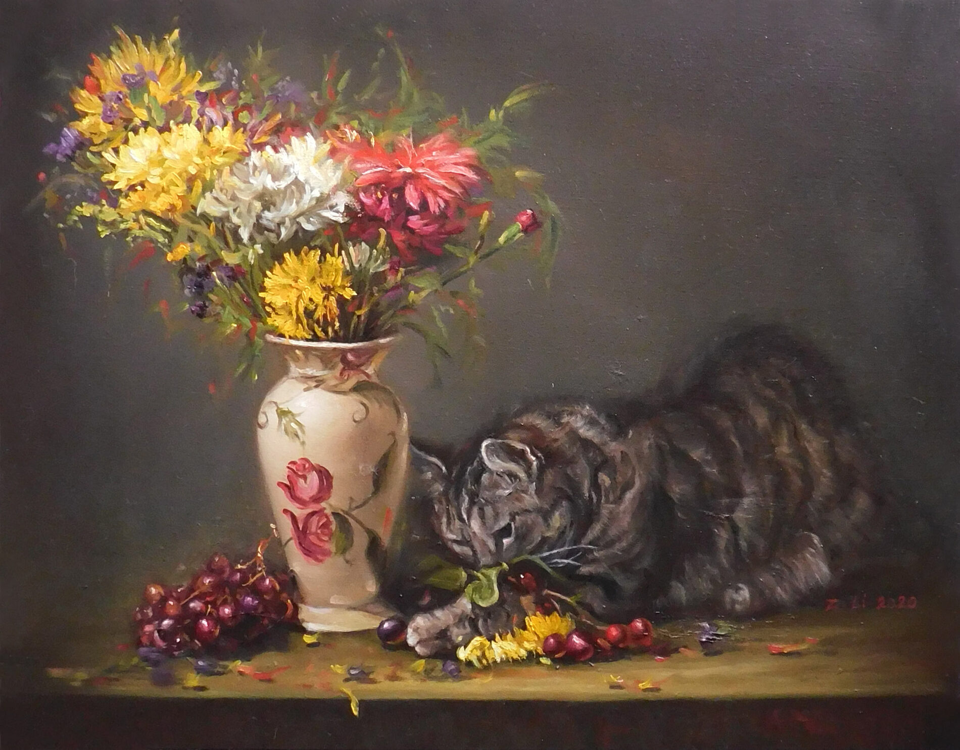 A cat plays with grapes and fallen flowers on a table next to a vase with assorted flowers.