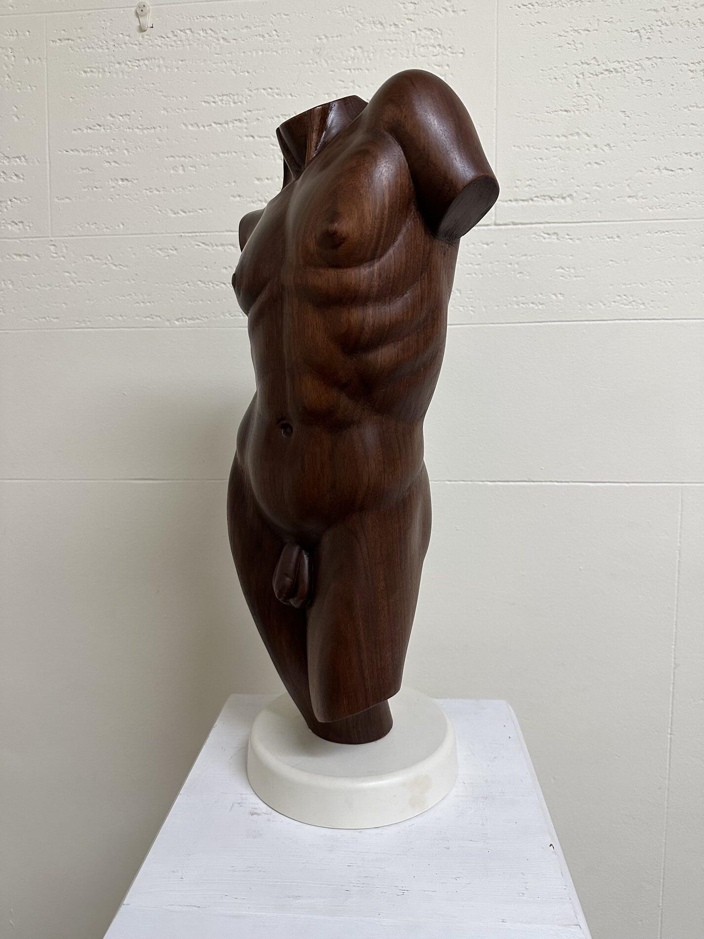 A wooden sculpture of a naked man on a pedestal.