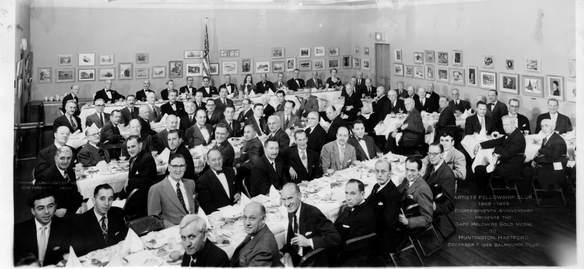 Restored photo: Rows of men in suits are cheerfully seated at long tables in a gallery space for dinner.