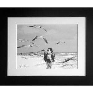 A black and white photo of a woman on the beach with seagulls.