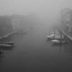 Black and white photo of a canal with boats docked in it.