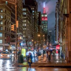 A city street at night with the empire state building in the background.