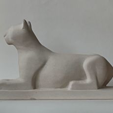 A white sculpture of a cat sitting on a block.