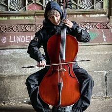 A man playing a cello in front of a building.