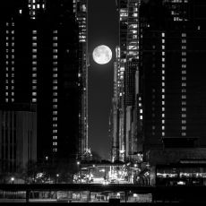 A black and white photo of the moon rising over the city.