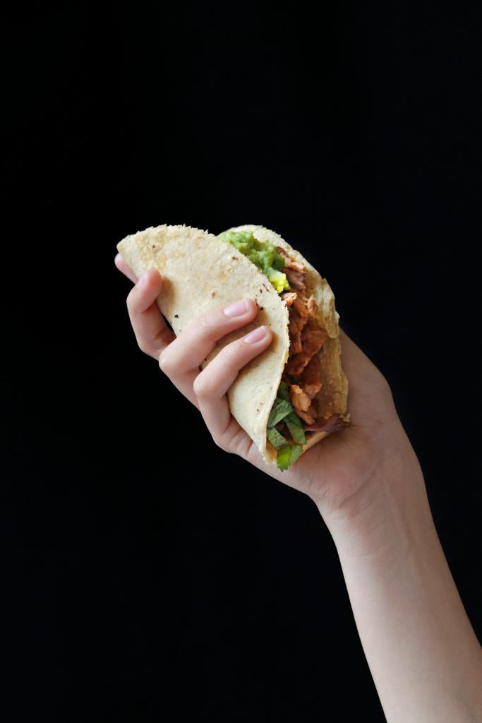 A hand holding a taco against a black background.